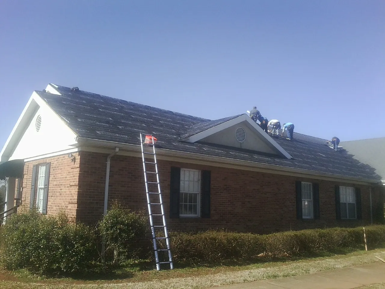 Crew tearing shingles off a brick ranch roof with a ladder set — Metal Roof Repair work by our crew in Hermanville