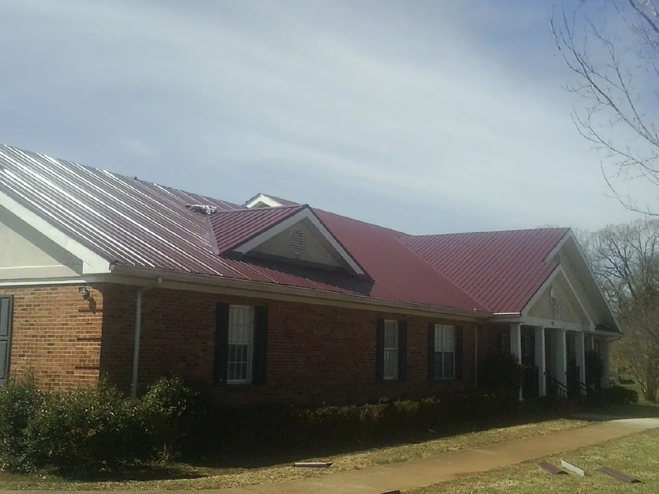 Red metal roof with gabled entries on a long brick building, from a Hail Damage Roof Repair job in Hermanville
