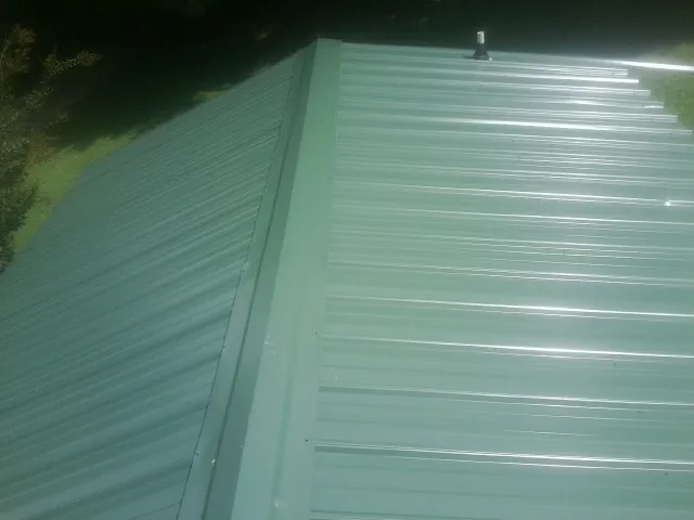 New green metal panels meeting at the ridge of a roof — Flat Roof Repair work by our crew in Hermanville