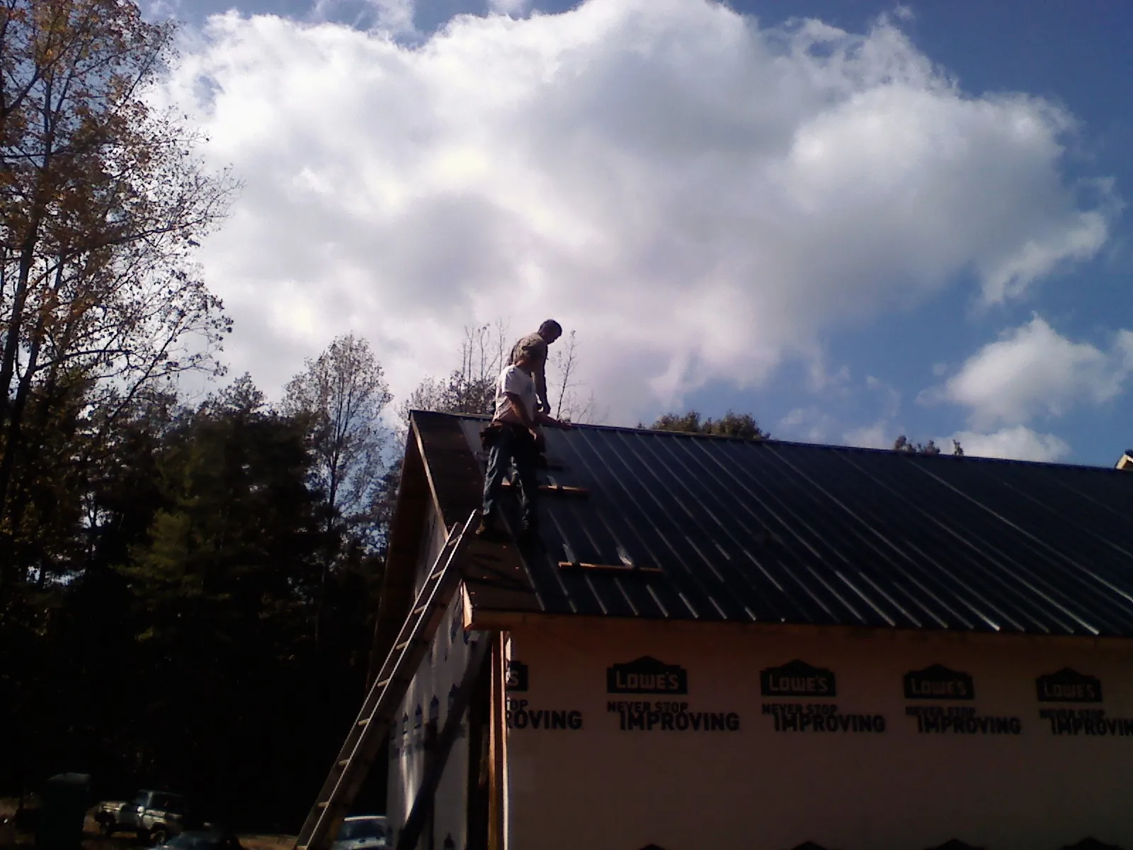 Roofer fastening dark metal panels high against a cloudy sky, from a Roof Inspection job in Hermanville