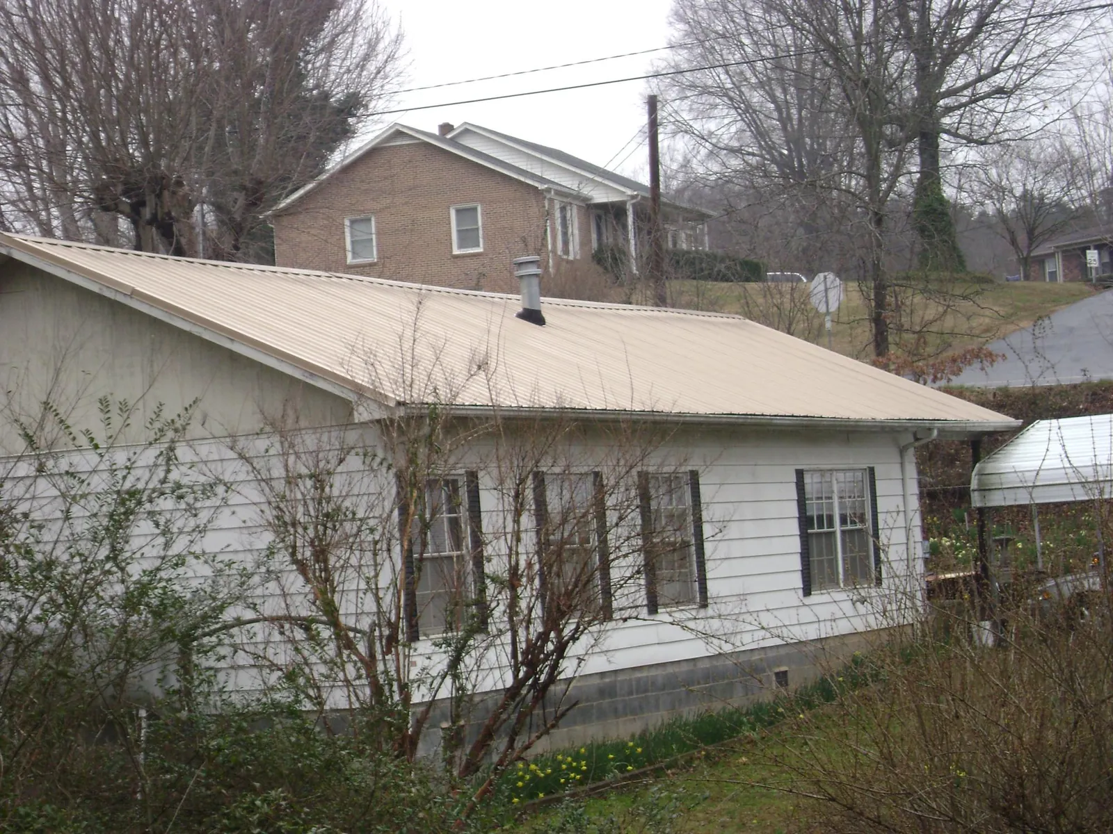 Tan metal roof on a white sided house set into a hillside — Commercial Roofing by Roofing Brothers in Hermanville